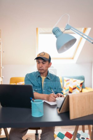 Foto de Foto vertical de un empresario casual concentrado escribiendo notas mientras trabaja en una oficina en casa - Imagen libre de derechos