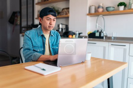 Photo for Morning scene of an asian man working with a laptop from the kitchen - Royalty Free Image