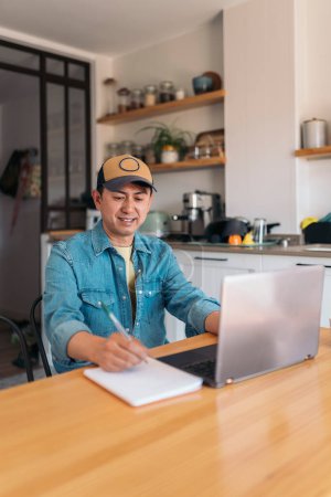 Téléchargez les photos : Photo verticale d'un homme d'affaires asiatique occasionnel utilisant un ordinateur portable tout en écrivant des notes et en travaillant à la maison - en image libre de droit