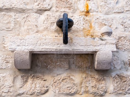 Téléchargez les photos : Rab, Croatie - 24 août 2022 : Un ancien anneau en métal coulé dans la marmite repose sur une étagère en pierre enchâssée dans un vieux mur d'architecture complexe. - en image libre de droit