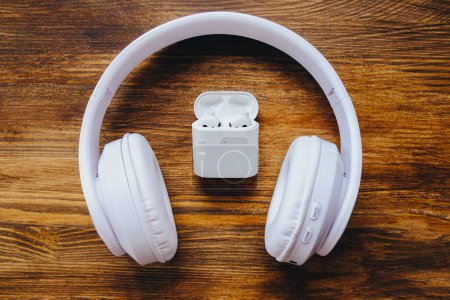 Photo for Full size big headphones vs small earbuds. Big and small white earphones on a wooden table. - Royalty Free Image