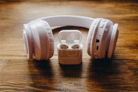 White headphones of different sizes on a wooden background. Small and large headphones.