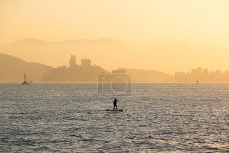 Photo for Boy practicing stand up paddle in the bay of Santos, Sao Paulo, Brazil. In the background, Porchat Island in Sao Vicente. - Royalty Free Image