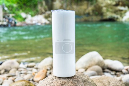 In this tranquil scene, a long tumbler is artfully displayed above a rock near the serene waters of the nearby river, adding a touch of sophistication to the setting, white blank long tumbler mockup image