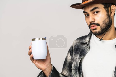 Photo for Effortlessly stylish, a mockup image captures the essence of promotion with a young bearded man highlighting a white blank wine tumbler in a minimalistic arrangement - Royalty Free Image