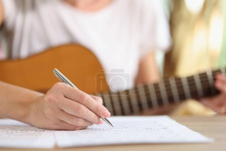 Foto de Primer plano de la mano femenina escribiendo notas de nueva canción. Nuevas ideas cantante inspirador componiendo música con guitarra en casa. Concepto de arte musical - Imagen libre de derechos