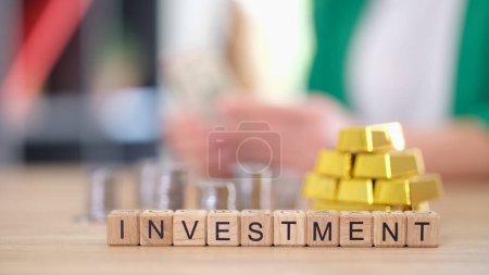 Word investment with gold bars and stacks of coins on table. Currency exchange rates, saving and investing money and diversification.