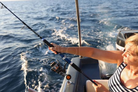 Foto de Retrato de mujer sosteniendo caña de pescar en las manos. Hembra tomando pescado de barco de motor. Concepto de pescado, pesquería y caña de pescado - Imagen libre de derechos