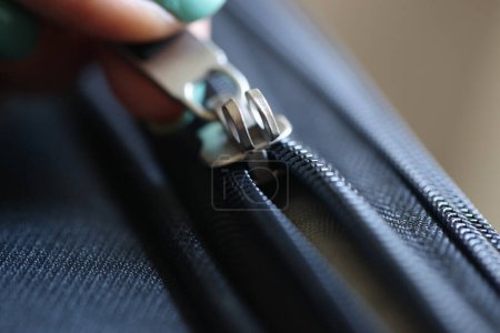 Photo for Close-up of female hand opening black brass zipper of suitcase. Metal zipper pulled by slider - Royalty Free Image