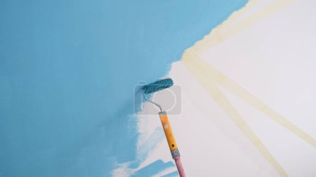 Téléchargez les photos : Gros plan du mur de peinture décorateur en couleur bleue et à l'aide de ruban scotch et rouleau. Réparation, rénovation et conception créative du concept de maison - en image libre de droit