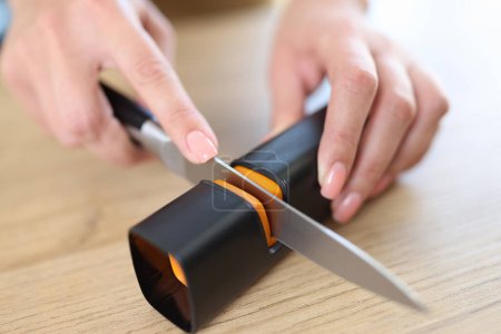Téléchargez les photos : Woman hands sharpen knife with sharpener on kitchen table close-up. Feminism and woman doing mens work concept. - en image libre de droit