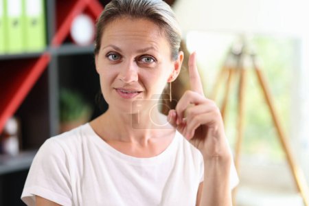 Photo for Close-up of shrewd smart woman in casual clothes. Female shows gesture with her index finger up. Symbol of insight and good idea. - Royalty Free Image