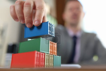 Business man arranging stack of cargo containers on his office desk. Logistics, shipping goods, export and import concept.