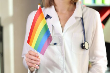 Ärztin hält Regenbogen-LGBT-Flagge in der Hand. Konzept der medizinischen Hilfe nach der Geschlechtsumwandlung.