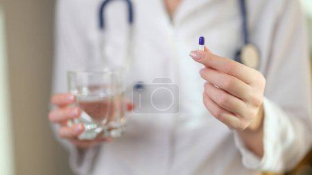 Doctor holds pill in one hand and glass of water in other. Medical treatment, right dose and health care concept.