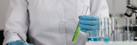 Foto de El investigador tiene un tubo de ensayo con datos de registros de líquidos verdes. Obtenido como resultado de un experimento químico en concepto de laboratorio - Imagen libre de derechos