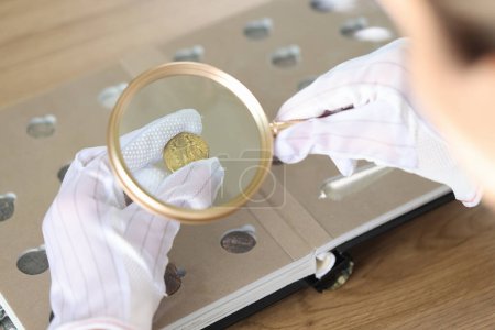 Photo for Close-up of woman numismatist examining coin with magnifier. Female looks at coins through loupe. Numismatic collection review - Royalty Free Image
