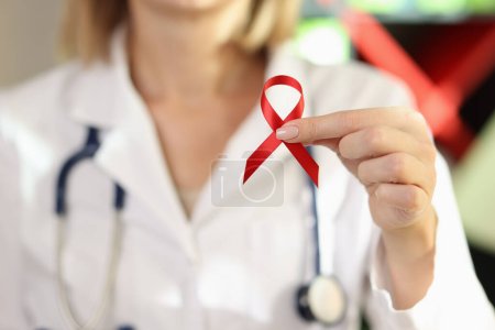 Woman doctor holding red ribbon as symbol of AIDS close up. International World Aids Day, HIV awareness concept.