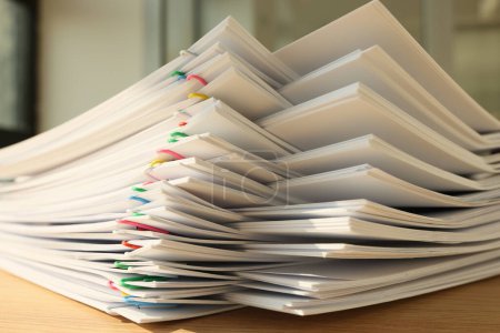 High stack of office documents with clips on office table close up. Concept of overworking and paperwork in office.