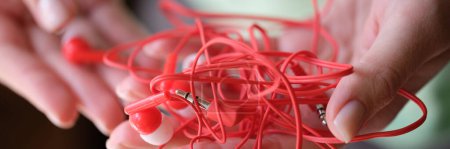 Photo for Close-up of woman holding red tangled earphone, headphones mess. Audio equipment for modern sound technologies - Royalty Free Image