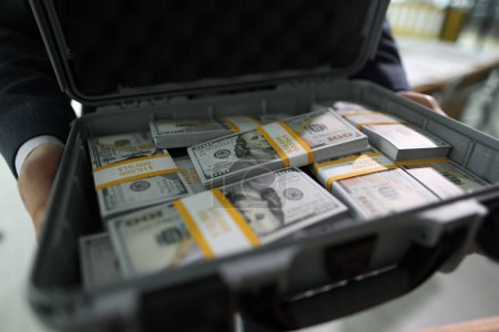 El gerente sostiene el caso abierto con pilas contadas de billetes de dólar en las manos. Hombre muestra maletín con dinero pagado por acuerdo exitoso por el cliente