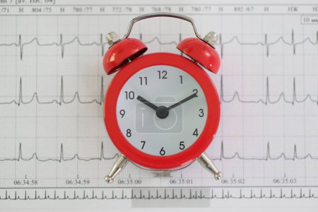 Foto de Reloj despertador vintage está contra el papel cardiograma en la clínica. Monitorización detallada de la frecuencia cardíaca en el hospital. Concepto de salud y esperanza de vida - Imagen libre de derechos
