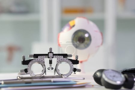 Lunettes utilisées pour le test de la vue sur table contre un modèle d'oeil réaliste flou. Équipement ophtalmologique professionnel dans le bureau de la clinique
