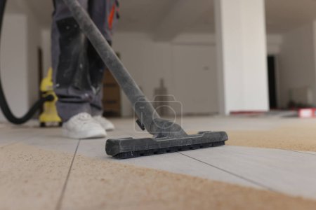 Foreman fait le nettoyage industriel du plancher stratifié dans la pièce au processus de rénovation. Aspirateurs homme sciure de sol avec appareil ménager moderne