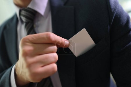 Foto de El hombre de negocios de traje saca la tarjeta de crédito del bolsillo del pecho de la chaqueta con la mano. El hombre exitoso proporciona dinero para hacer el pago por los servicios de negocios - Imagen libre de derechos