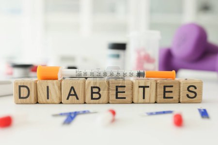 Word Diabetes mit Holzwürfeln und Spritze auf dem Tisch. Chronische endokrine Erkrankungen, die durch anhaltend hohe Blutzuckerspiegel verursacht werden. Insulinspritze