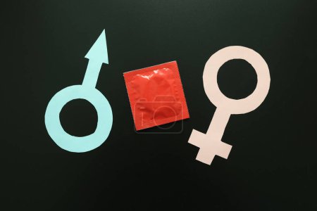 Foto de Símbolos masculinos y femeninos con condón sobre fondo negro. Contactos sexuales seguros y concepto anticonceptivo. Protección para parejas íntimas - Imagen libre de derechos