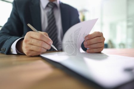 Confident male employee flips page of contract signing after reading. Man in classic suit puts signature on paper sheet making important decision in company