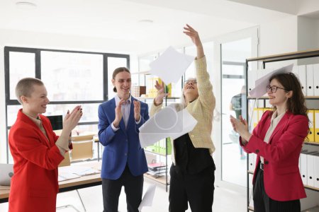 Photo for Mature lady employee throws up papers while colleagues applaud in company office. Happy workers celebrate finish of complicated business project - Royalty Free Image
