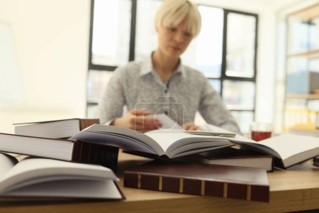 Femme aux cheveux courts recherche des informations dans des livres épais pour le travail des diplômés assis à table dans la bibliothèque lumineuse. Étudiante acquiert des connaissances pour la croissance de carrière