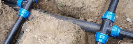 Téléchargez les photos : Close-up of underground irrigation system, plumbing water drainage installation. Elbow fitting and pvc pipes at bend in dirt trench outdoors - en image libre de droit