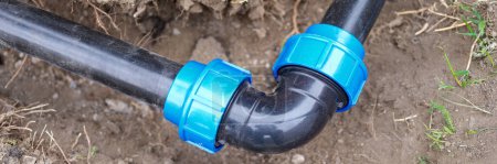 Téléchargez les photos : Close-up of elbow fitting and black pvc pipes at bend in trench outdoors. Plumbing water drainage installation. Underground irrigation system concept - en image libre de droit