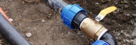 Close-up of plumbing water drainage installation in trench of ground. Underground irrigation system with elbow fitting of pvc pipes at bend with yellow tap or faucet