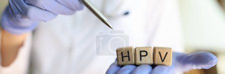 Close-up of doctor hands holding wooden cubes with word hpv. Practitioner pointing with pen on collected word. Human papillomavirus acronym