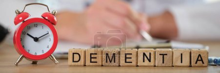 Close-up of dementia word collected of wooden cubes in row and alarm clock. Decrease in cognitive activity and memory. Emotional problems and brain diseases