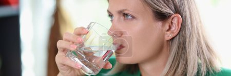 Photo for Close-up of unhappy woman with serious face drinking of non-carbonated water. Dehydration, health problems and stress concept. - Royalty Free Image