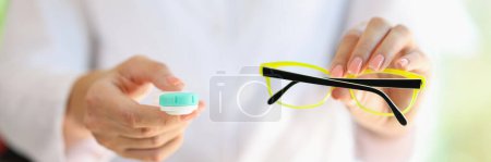Foto de El médico oftalmólogo sostiene anteojos y lentes de contacto en sus manos de cerca. Concepto de elección entre lentes y gafas y recomendaciones del optometrista. - Imagen libre de derechos