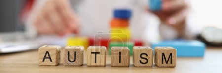 Word autism assembled from wooden blocks close-up and psychiatrist doctor with colored blocks at clinic table in background.