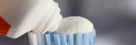 Téléchargez les photos : Presser du dentifrice blanc sur la brosse à dents. Tube de pâte à dents et brosse à dents avec poils bleus fermer. Concept de soins dentaires. - en image libre de droit