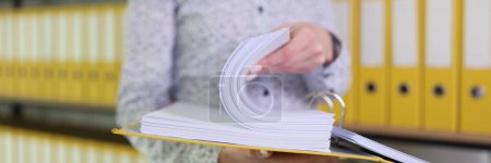 Female employee looks for accounting papers in ring binder. Woman stands against organized folder structure and archive in office closeup