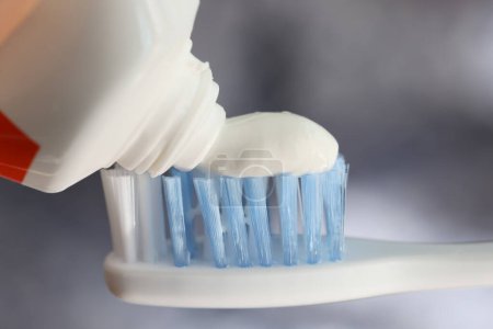 Téléchargez les photos : Presser du dentifrice blanc sur la brosse à dents. Tube de pâte à dents et brosse à dents avec poils bleus fermer. Concept de soins dentaires. - en image libre de droit