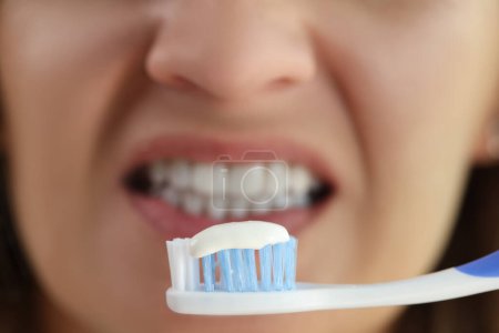 Toothpaste on toothbrush in front of womans face with white teeth close-up. Concept of hygiene, dental care and whitening.