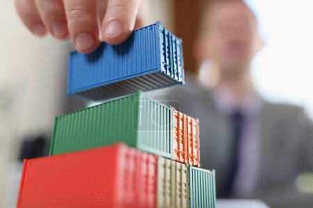Business man arranging stack of freight containers on his table in office. Logistics, freight transportation and trading worldwide. Imports, export and international distribution concept.