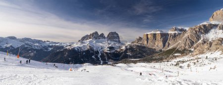 Dieses Bild fängt Skifahrer ein, die die Pisten inmitten einer schneebedeckten Bergkette unter klarem Himmel genießen. Die orangefarbenen Kegel markieren das Skigebiet und die majestätischen Berge dienen als atemberaubende Kulisse.