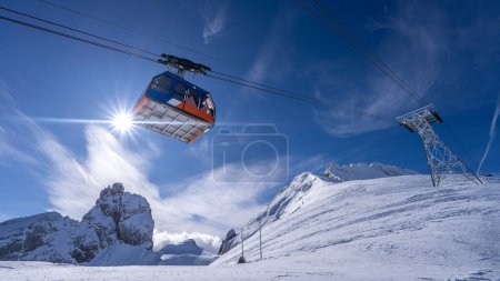 A breathtaking view of snowy peaks and a cable car under a bright sky in the Italian Alps. The pristine snowfield in the foreground glistens in the sunlight, creating a serene atmosphere.