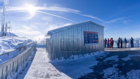 Téléchargez les photos : Une vue captivante depuis le paysage enneigé de San Pellegrinos sous un ciel bleu clair, avec des skieurs près d'une planche d'information et des sommets montagneux escarpés baignés de soleil au loin. - en image libre de droit